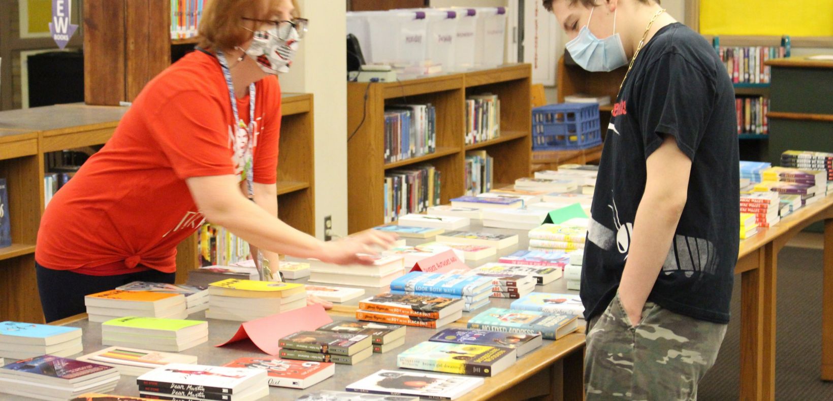 librarian helping student pick a book from a table of books