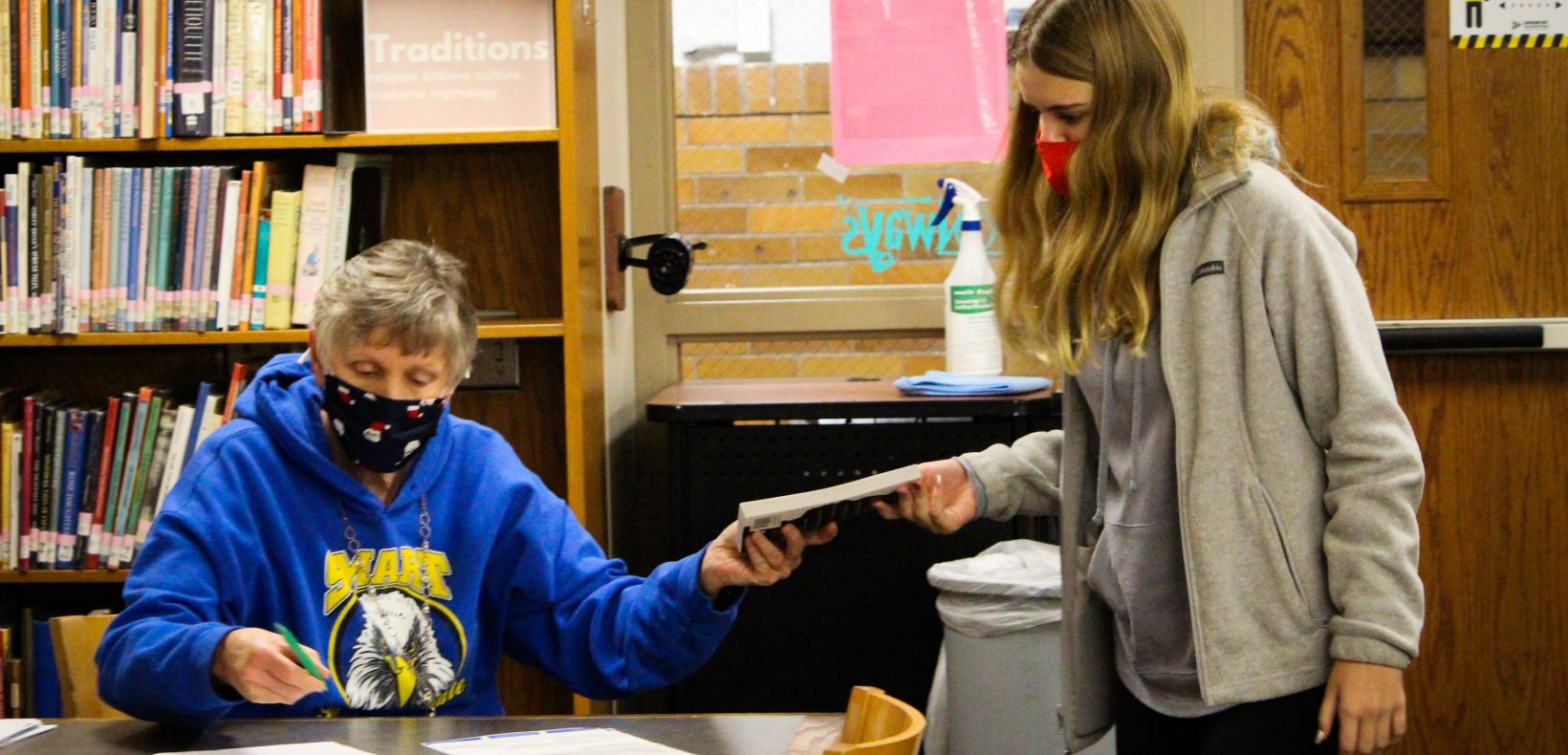 student handing a book to a clerk